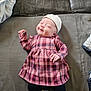 baby, newborn, infant, plaid_dress, beanie, hat, smile, couch, sofa, blanket, indoor, lying_down, socks, legs, cute, portrait, fabric, cozy, hand, small_person