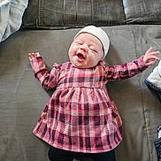 Kélya a rejoint le concours — aidez-le/la à gagner de superbes lots ! baby, infant, newborn, smiling, face, hat, plaid_dress, dress, socks, leggings, arms_up, lying_down, couch, blanket, fabric, home_interior, portrait, happy, soft_lighting, cute