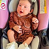 baby, infant, child, car_seat, vehicle, pink, brown_outfit, dress, hair_bow, white_booties, sitting, lying_down, open_mouth, smiling, portrait, indoor, car_interior, safety_labels, hands, feet