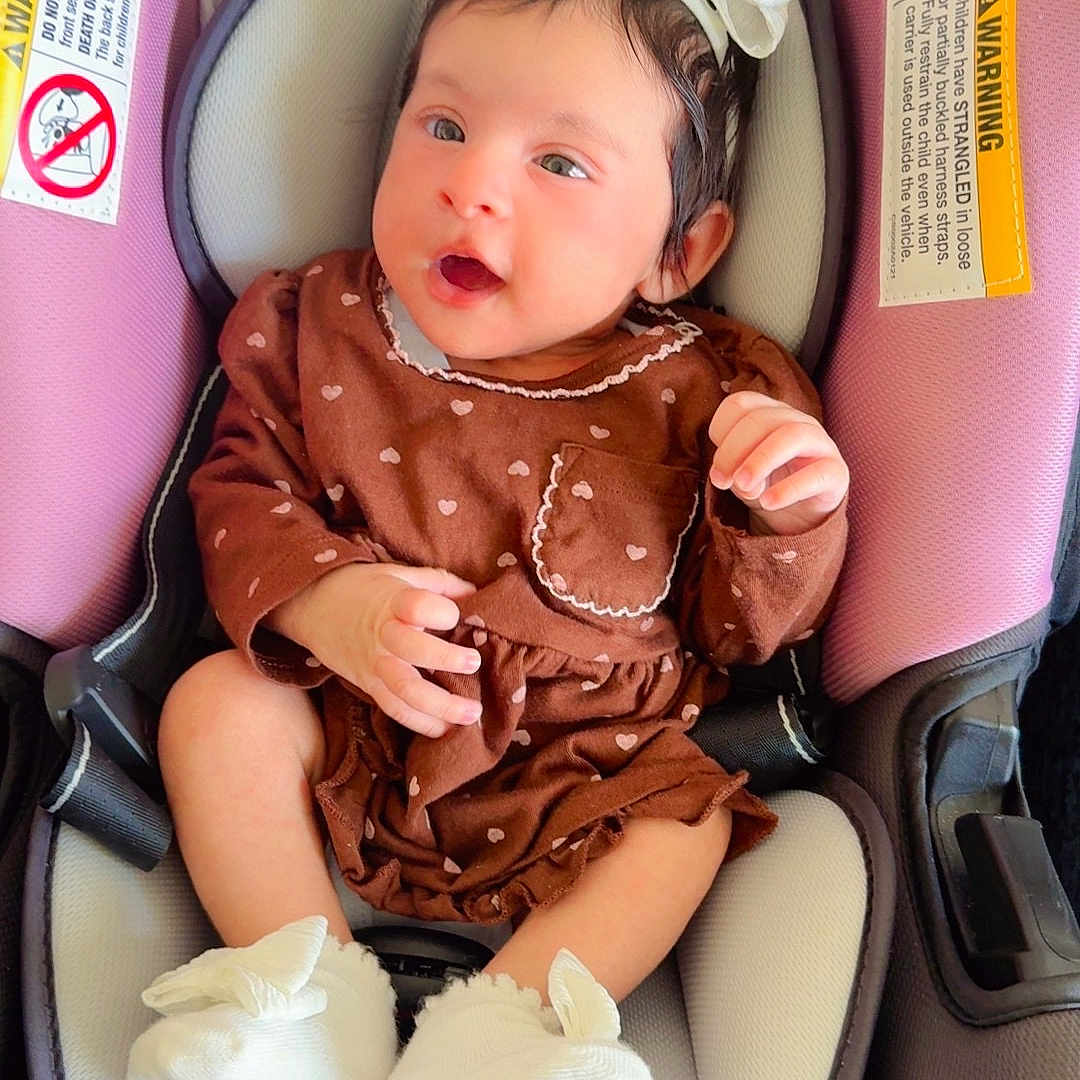 Abigail joined the competition — help win amazing prizes! baby, infant, child, car_seat, vehicle, pink, brown_outfit, dress, hair_bow, white_booties, sitting, lying_down, open_mouth, smiling, portrait, indoor, car_interior, safety_labels, hands, feet