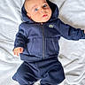 baby, child, infant, blue_hoodie, blue_pants, blanket, soft_texture, lying_down, indoor, cute, face, head, barefoot, clothing, portrait, young_child, casual_wear, curious_expression, skin, person