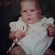 Ashley joined the competition — help win amazing prizes! baby, infant, candy_cane, white_clothing, frilly_outfit, serious_expression, sitting, portrait, indoor, child, cute, small_hands, young, face, head, skin, person, vintage_photo, dark_background, closeup