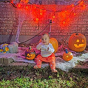 Azul joined the competition — help win amazing prizes! baby, child, pumpkin, jack_o_lantern, halloween, orange_lights, cobweb, brick_wall, grass, outdoor, festive, glowing, costume, holiday, decoration, cute, smiling, sitting, night, celebration