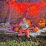 baby, child, pumpkin, jack_o_lantern, halloween, orange_lights, cobweb, brick_wall, grass, outdoor, festive, glowing, costume, holiday, decoration, cute, smiling, sitting, night, celebration