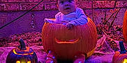 Azul is registered to the contest to win money with this photo: baby, pumpkin, jackolantern, halloween, glowing, carved, face, child, costume, outdoor, decorations, cobweb, spooky, festive, brick_wall, night, purple_lighting, cute, sitting, holiday