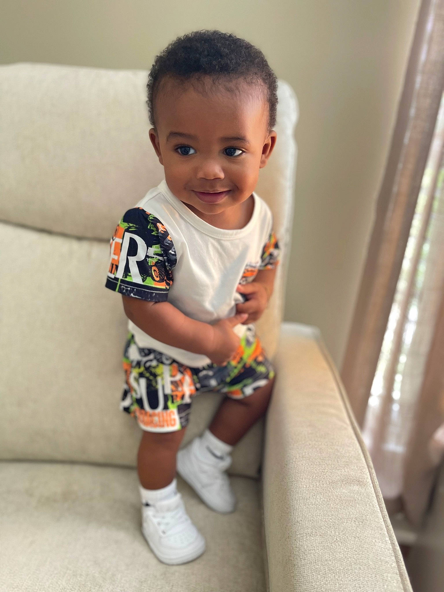 Rico joined the competition — help win amazing prizes! baby, baby_toddler_clothing, child, curtain, dress, facial_expression, flooring, happy, head, human_leg, knee, pattern, person, shorts, sitting, skin, sleeve, smile, sock, t_shirt