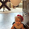 balloon, cabinet, child, crawling, curly_hair, cute, exploration, flooring, furniture, headband, home, indoor, person, playful, red_headband, string, toddler, white_balloon, wooden_floor, young_child