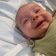 Finley is registered to the contest to win money with this photo: baby, smiling, face, closeup, infant, child, bed, bedding, white, clothing, green, ribbed, portrait, happy, cute, lying_down, skin, eyes, mouth, cheeks