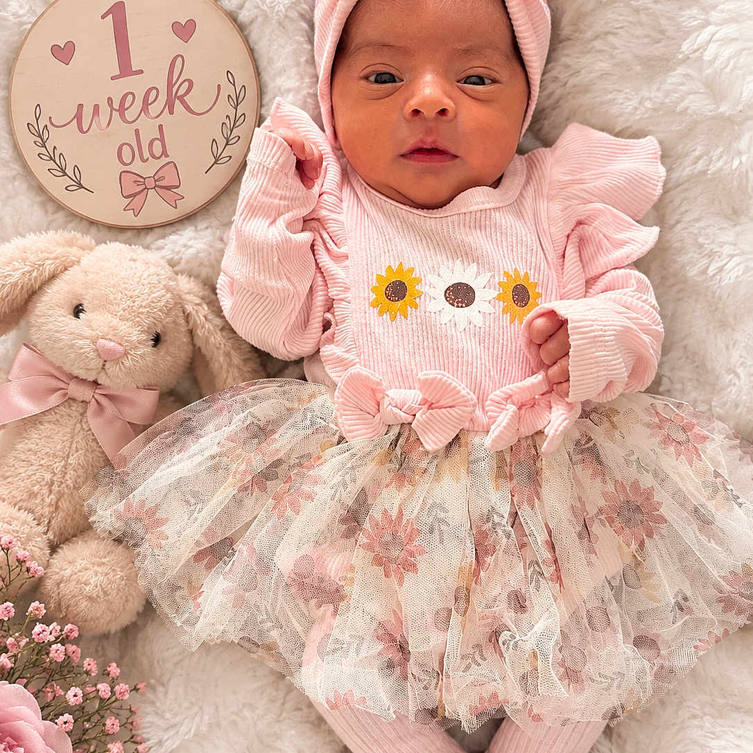 Jaelani is registered to the contest to win money with this photo: baby, newborn, infant, child, portrait, pink, headwrap, bow, floral_dress, tutu, blanket, teddy_bear, stuffed_animal, flowers, milestone_sign, one_week_old, lying_down, indoor, soft_lighting, cute