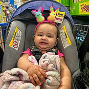 Ariyah is registered to the contest to win money with this photo: baby, blanket, bunny_ears, car_seat, child, clothing, colorful, comfort, cute, face, headband, indoor, infant, person, retail, shopping_cart, smile, soft, store, toy