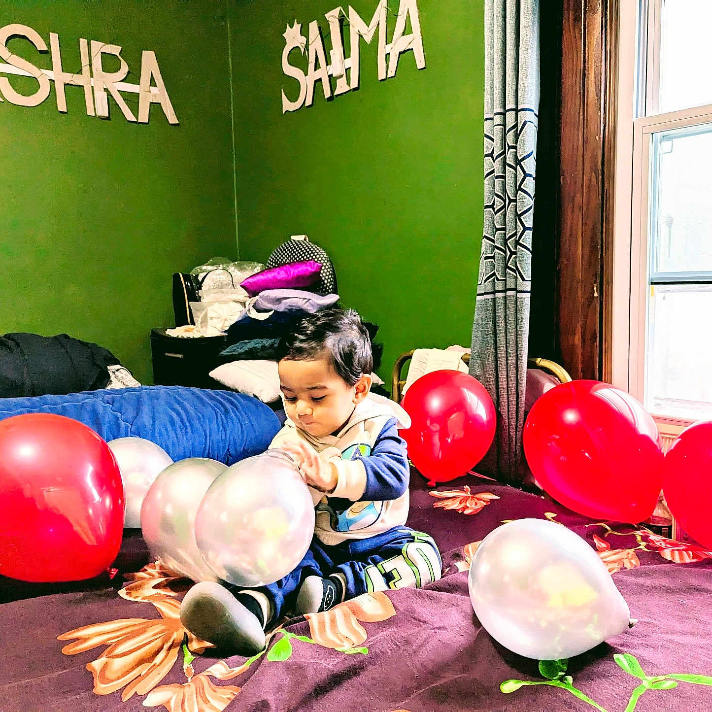 Shadab is registered to the contest to win money with this photo: balloon, bed, blanket, celebration, child, clothing, curtain, floor, furniture, green_wall, indoor, light, person, pillow, play, room, sitting, toddler, toy, window