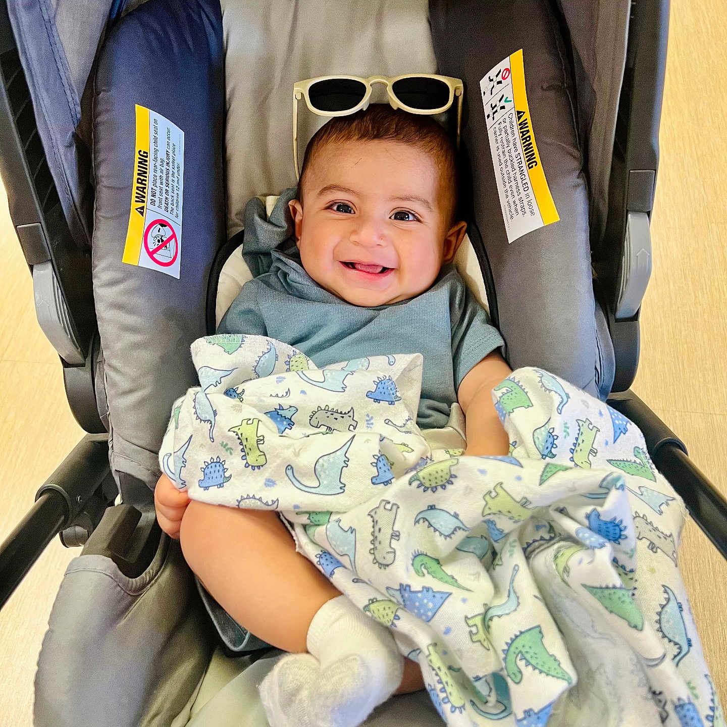Nathan joined the competition — help win amazing prizes! baby, car_seat, blanket, dinosaur_pattern, sunglasses, smile, happy, infant, child, cute, feet, socks, clothing, indoor, floor, person, portrait, seat, headwear, comfort