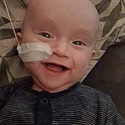 Flynn is registered to the contest to win money with this photo: baby, smiling, face, nasaltube, lyingdown, striped_clothing, pillow, infant, happy, child, cute, healthcare, medical, indoors, person, portrait, head, skin, eyes, mouth