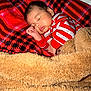 baby, sleeping, blanket, red_plaid, fleece, striped_clothing, cozy, infant, cute, portrait, indoor, resting, child, soft_texture, warm, peaceful, hand_near_face, head, face, comfort