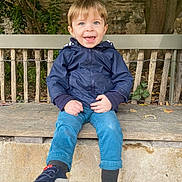 Malo participe au concours pour gagner de l'argent avec cette photo : child, toddler, smiling, blue_eyes, jacket, pants, sneakers, bench, outdoor, tree, leaves, wood, stone, happy, person, casual_clothing, nature, daylight, cute, playful