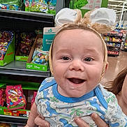 Dustin is registered to the contest to win money with this photo: baby, child, bunny_ears, smile, drool, onesie, dinosaur_print, hand, store, aisle, candy, easter, toys, shelf, packaging, person, holding, cute, happy, indoor