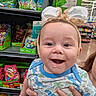 baby, child, bunny_ears, smile, drool, onesie, dinosaur_print, hand, store, aisle, candy, easter, toys, shelf, packaging, person, holding, cute, happy, indoor