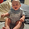 Dustin is registered to the contest to win money with this photo: baby, barefoot, bed, blue_checkered_shirt, child, clothing, face, feet, happy, head, indoors, legs, person, pillow, room, sitting, smiling, striped_sheets, television, young_child