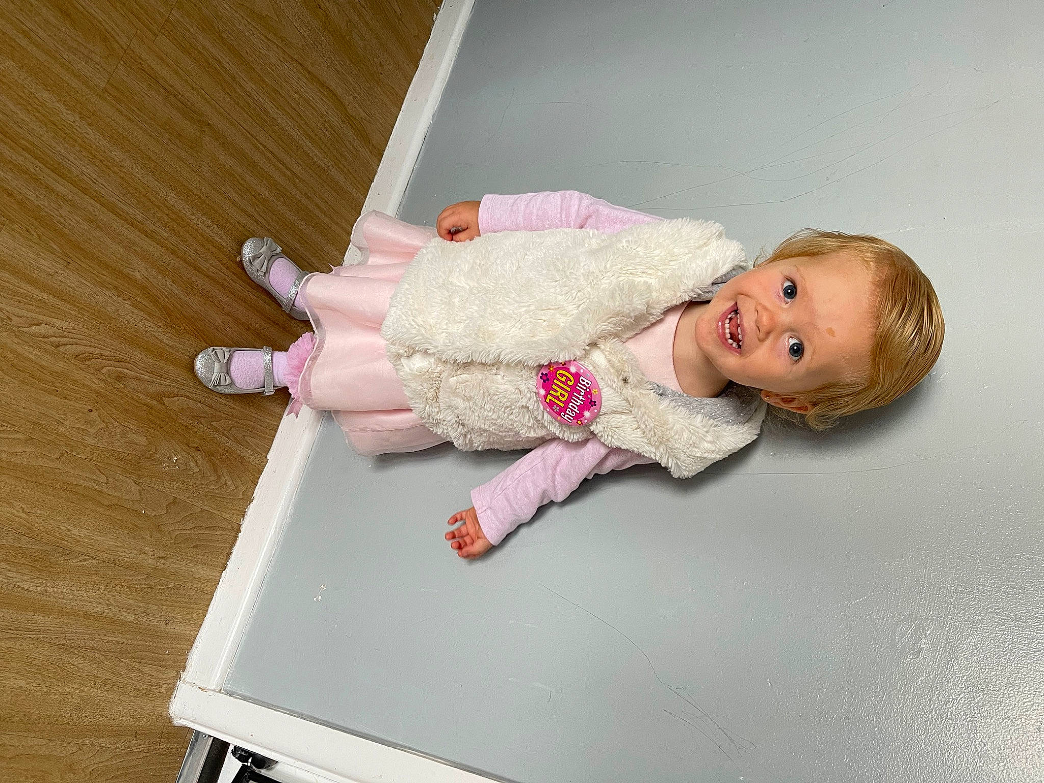 Evie-mae is registered to the contest to win money with this photo: arm, baby, baby_toddler_clothing, cheek, child, comfort, facial_expression, floor, flooring, hardwood, joint, leg, magenta, person, room, skin, sleeve, smile, sock, toddler