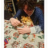person, dog, table, hot_chocolate, cup, stirring, tablecloth, holiday, festive, indoor, cozy, fluffy_dog, pomernian, blue_clothing, hair, face, hands, warm, food, drink