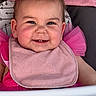 baby, child, smiling, face, earrings, party_hat, pink_clothing, bib, high_chair, cute, cheeks, portrait, happy, indoor, infant, toddler, clothing, sitting, headwear, closeup
