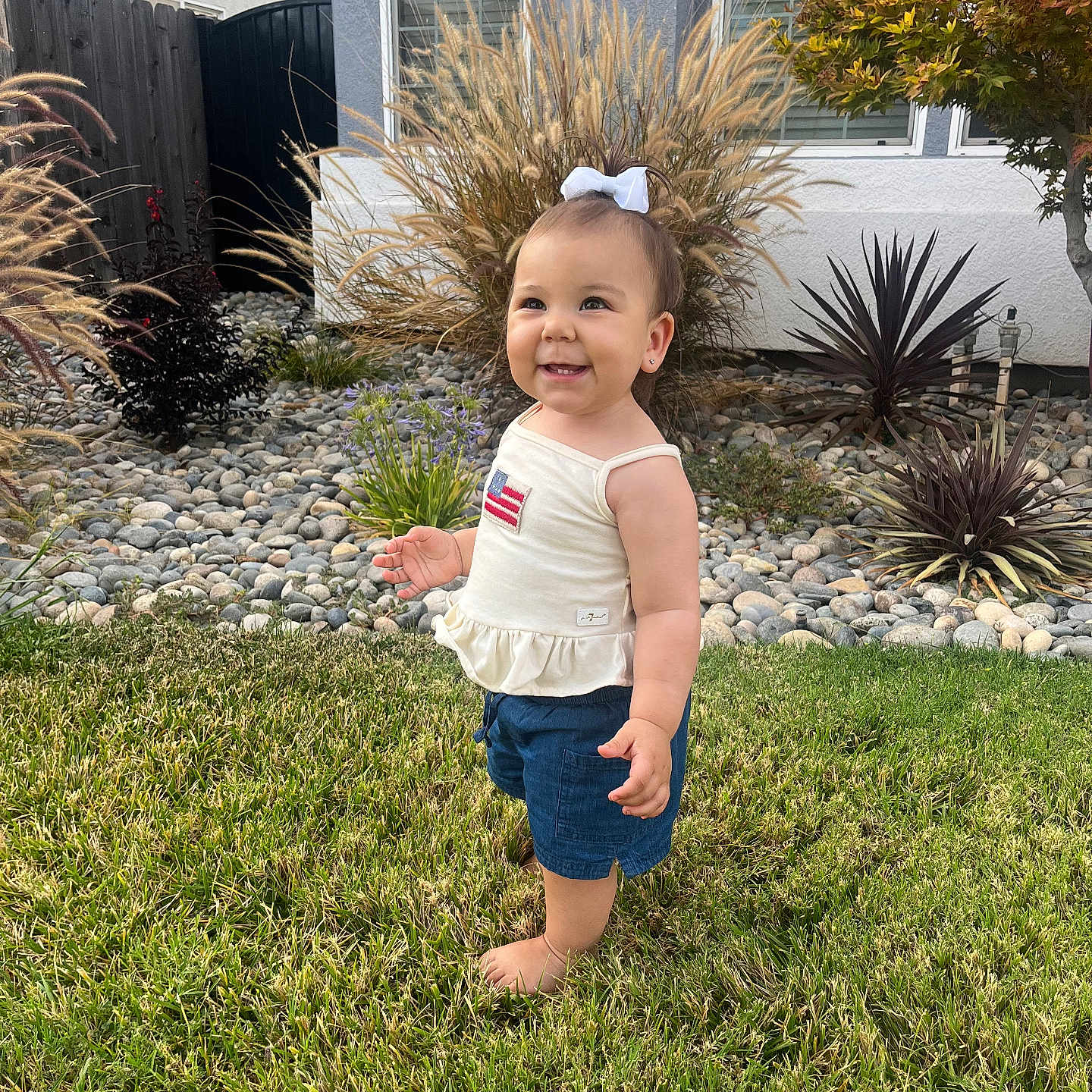 Amarosa joined the competition — help win amazing prizes! toddler, child, grass, lawn, garden, plants, rocks, house, window, white_bow, tank_top, shorts, barefoot, smiling, outdoor, daylight, happy, portrait, nature, suburban