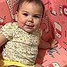 baby, child, smiling, sitting, floral_clothing, yellow_shorts, pink_background, animal_print, face, cute, happy, indoors, earrings, portrait, infant, bright_colors, young_child, playful, decor, person