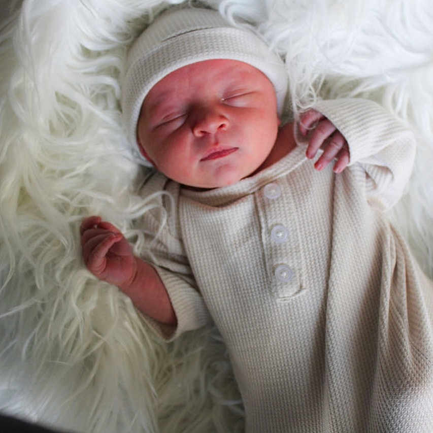 Saint is registered to the contest to win money with this photo: baby, blanket, child, clothing, cozy, cute, fur, hat, indoors, infant, knitwear, newborn, peaceful, portrait, resting, sleep, sleeping, small_hands, soft_texture, warm