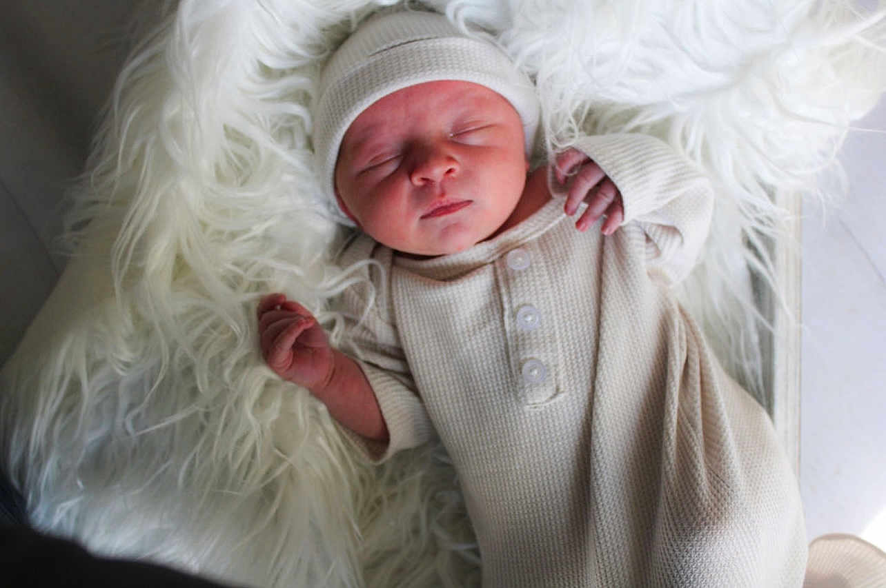 Saint is registered to the contest to win money with this photo: newborn, baby, sleeping, infant, knitwear, hat, blanket, fur, cozy, soft_texture, peaceful, portrait, child, indoors, cute, resting, sleep, small_hands, clothing, warm
