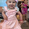 Heidi joined the competition — help win amazing prizes! baby, child, girl, smiling, pink_dress, headband, flower, indoor, kitchen, floor, shoes, socks, person, holding, furniture, background, young_girl, toy, drink, family