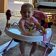 Heidi is registered to the contest to win money with this photo: baby, infant, baby_walker, pink_clothing, smiling, indoor, carpet, rocking_chair, blanket, toy, window, door, daylight, furniture, foot, person, child, happy, play, living_room