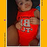 baby, baby_girl, child, closeup, cute, face, frame, hand, heart_emoji, indoors, infant, looking_up, person, portrait, red_clothing, skin, smile, text_overlay, yellow_background, young_child