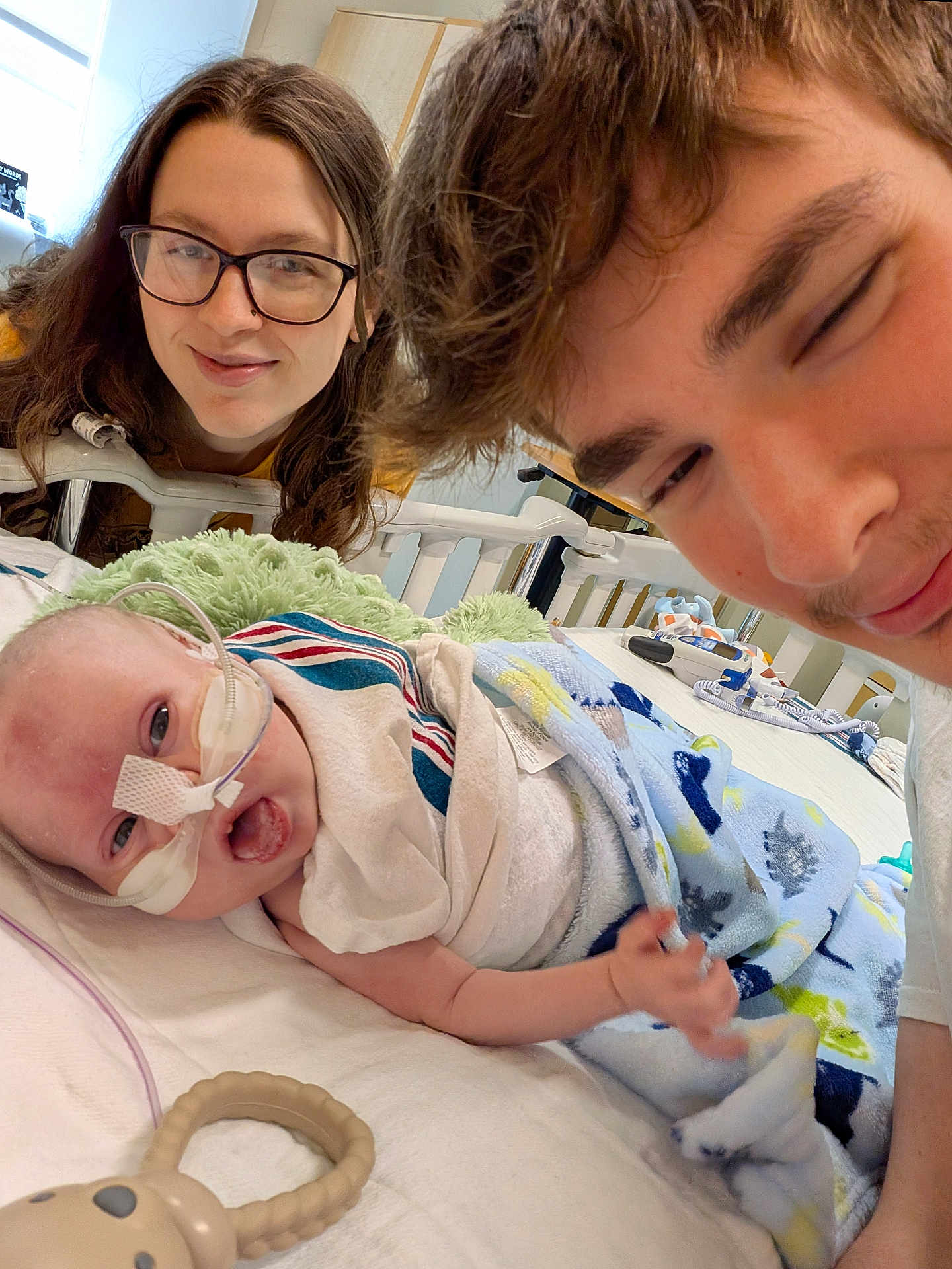 Raymond joined the competition — help win amazing prizes! baby, infant, hospital, medical_tube, blanket, adult, glasses, smile, bed, toy, healthcare, care, family, cozy, person, indoor, portrait, happy, lying_down, parent