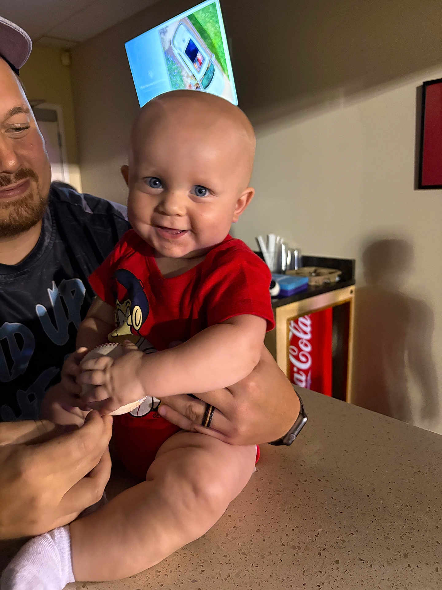 Memphis joined the competition — help win amazing prizes! baby, child, infant, smiling, holding, baseball, person, adult, indoor, counter, television, fridge, coca_cola, red_clothing, sock, hand, face, happy, casual, home