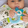 baby, infant, teething_toy, blue_eyes, mickey_mouse_print, clothing, hand, face, person, closeup, cute, child, sitting, comfort, soft_toys, parent, white_tank_top, playful, indoor, portrait