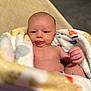 baby, infant, blanket, naked_torso, face, tongue, skin, hand, cushion, seated, indoors, soft_texture, comfort, cute, child, newborn, expression, relaxation, portrait, cozy