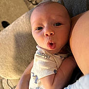 J.j. is registered to the contest to win money with this photo: baby, infant, face, expression, surprised, person, arm, clothing, onesie, indoor, couch, blanket, skin, head, eyes, mouth, hand, closeup, human, babywear