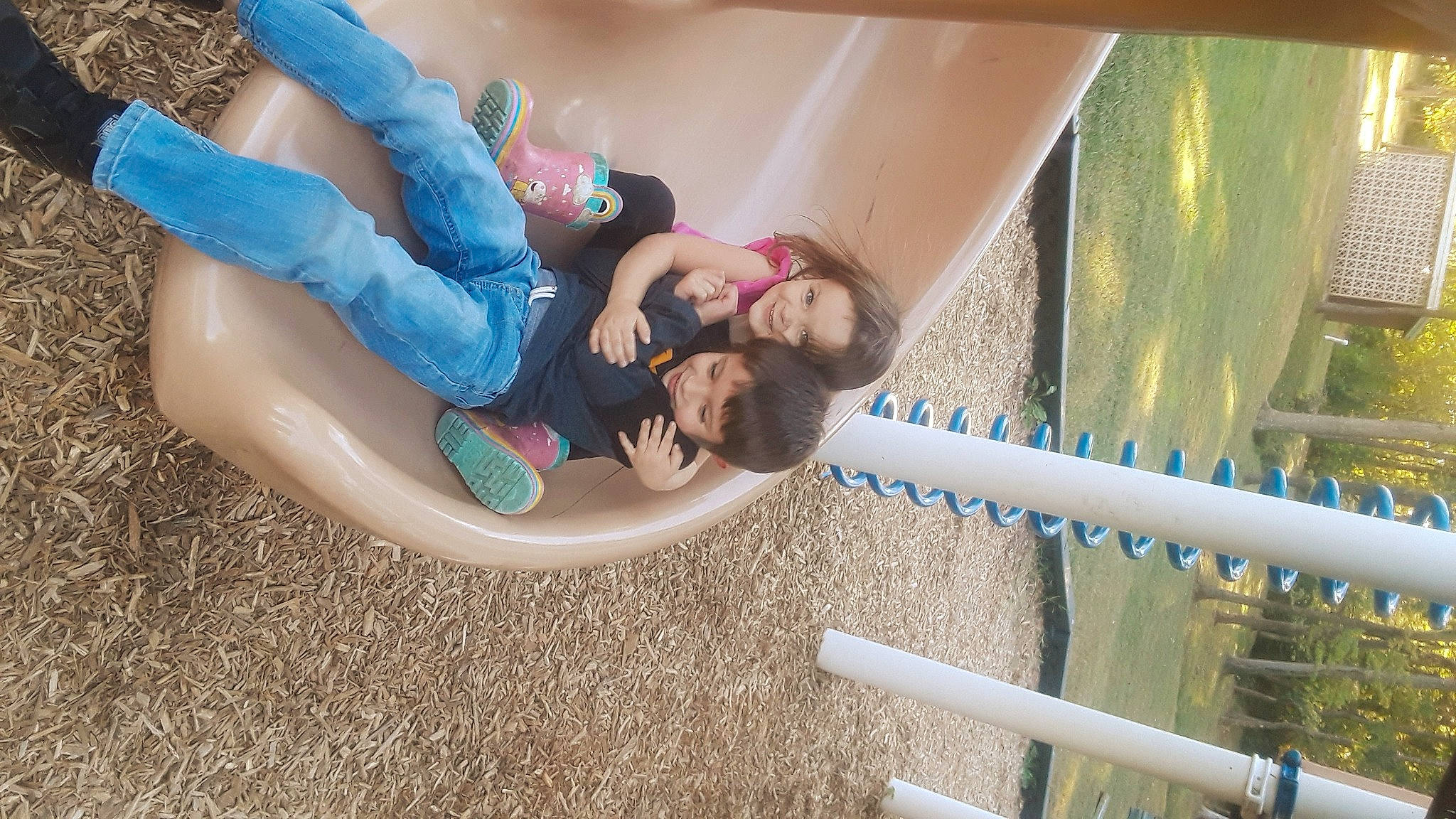 Kira is registered to the contest to win money with this photo: child, city, comfort, fun, grass, happy, human_leg, joy, knee, leisure, outdoor_play_equipment, person, plant, playground_slide, public_space, recreation, sitting, smile, t_shirt, thigh