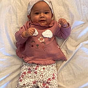 Zoey joined the competition — help win amazing prizes! baby, child, infant, pink_clothing, headband, bow, patterned_pants, lying_down, bed, blanket, smiling, happy, cute, small_hands, footwear, indoors, portrait, young_child, soft_fabric, casual