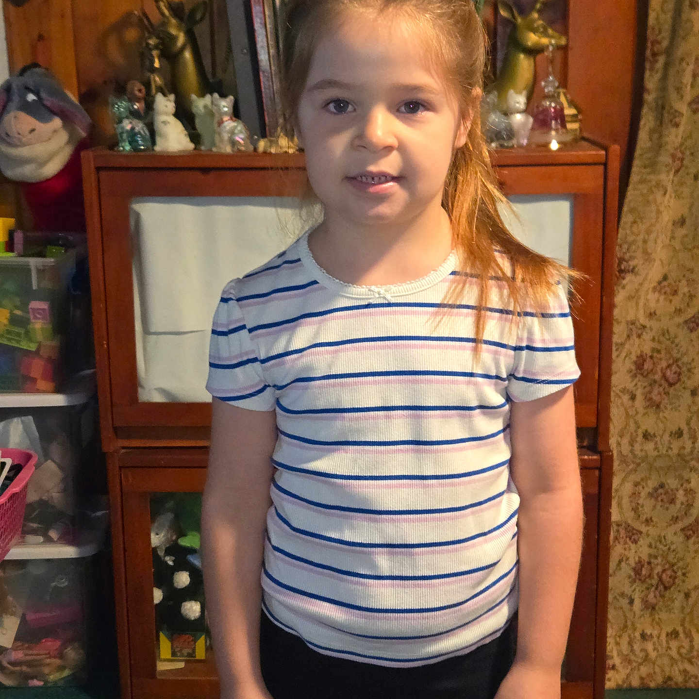 Jessie-Lynn joined the competition — help win amazing prizes! child, girl, portrait, standing, smiling, striped_shirt, ponytail, hair_bow, indoors, home, cabinet, furniture, figurines, decorations, mirror, curtain, carpet, collection, front_facing, photograph