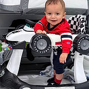 Asher is registered to the contest to win money with this photo: baby, toddler, child, smile, baby_walker, toy_car, racing_wheel, checkered_pattern, red_sweater, crib, indoor, playtime, portrait, face, hand, socks, blanket, floor, happy, toy