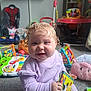 Hallie joined the competition — help win amazing prizes! baby, child, curly_hair, pigtails, purple_clothing, book, toy, playroom, carpet, plush_toy, smiling, indoors, childhood, happy, infant, colorful, floor, person, cute, learning