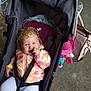 Hallie is registered to the contest to win money with this photo: baby, child, stroller, curly_hair, smiling, thumb_in_mouth, colorful_jacket, floral_pattern, leggings, seatbelt, pink_bag, toy, outdoor, path, blurred_background, person, cute, happy, infant, portrait