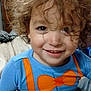 child, toddler, curly_hair, smiling, blue_shirt, orange_bow_tie, orange_suspender, bed, blanket, indoor, portrait, happy, cute, person, face, young_child, casual_clothing, closeup, playful, cozy