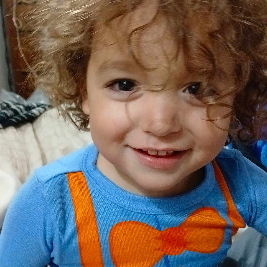 Lalo joined the competition — help win amazing prizes! bed, blanket, blue_shirt, casual_clothing, child, closeup, cozy, curly_hair, cute, face, happy, indoor, orange_bow_tie, orange_suspender, person, playful, portrait, smiling, toddler, young_child