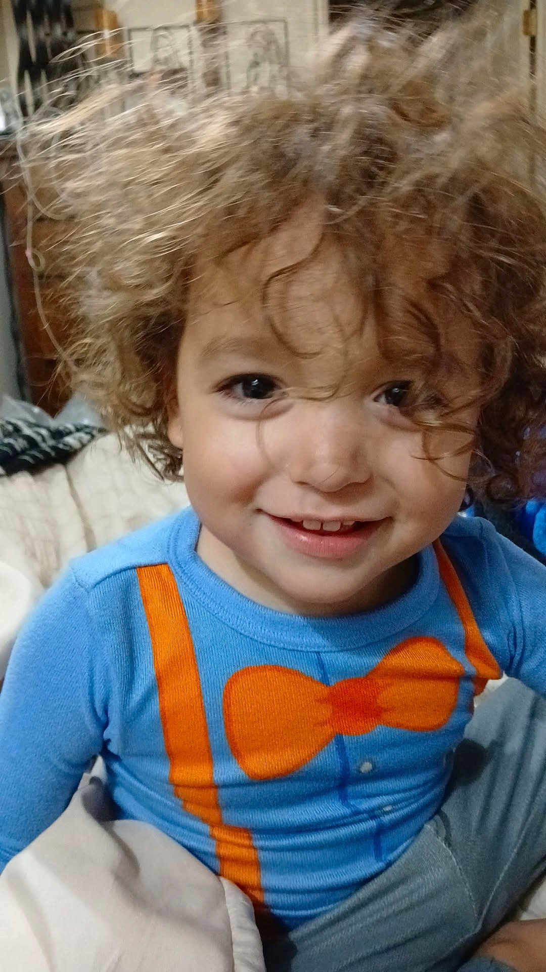 Lalo joined the competition — help win amazing prizes! child, toddler, curly_hair, smiling, blue_shirt, orange_bow_tie, orange_suspender, bed, blanket, indoor, portrait, happy, cute, person, face, young_child, casual_clothing, closeup, playful, cozy