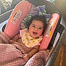Olivia is registered to the contest to win money with this photo: baby, infant, smiling, pink_blanket, car_seat, bib, indoor, living_room, couch, blanket, happy, child, person, face, soft_texture, cozy, cute, comfort, warm_light, seated