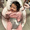 baby, smiling, pink_onesie, face, infant, child, seat, cushion, toy, hanging_toy, happy, indoor, floor, checkered_floor, hair, person, cute, cozy, laughing, baby_seat