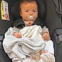 baby, blanket, bundle, car_seat, caution_label, child, closeup, clothing, cute, face, footwear, head, indoors, infant, pacifier, person, safety, seatbelt, sitting, young