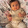 baby, infant, child, blanket, floral_pattern, clothing, pants, shirt, polka_dots, face, eyes, hands, feet, socks, bedroom, soft_lighting, curious_expression, indoor, portrait, cute